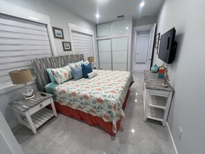 Un dormitorio con cama, mesitas de noche, televisión y armario.