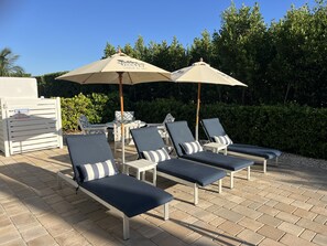 Un espace aménagé au bord de la piscine, avec des chaises longues et des parasols, un panneau d’avertissement et une haie en arrière-plan.