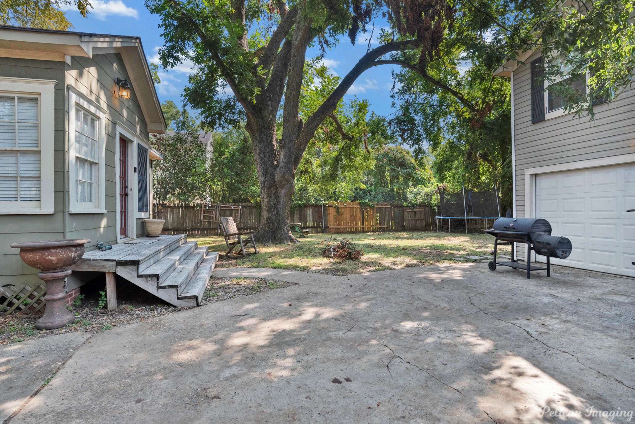 A backyard with a wooden deck, a barbecue grill, and a large tree.