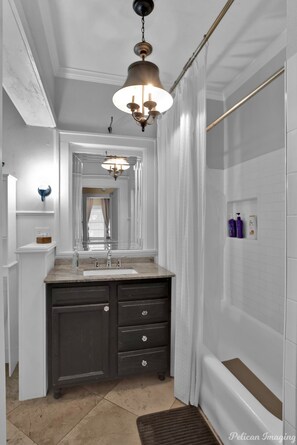 A bathroom with a white vanity, a mirror, a shower, and a ceiling light fixture.