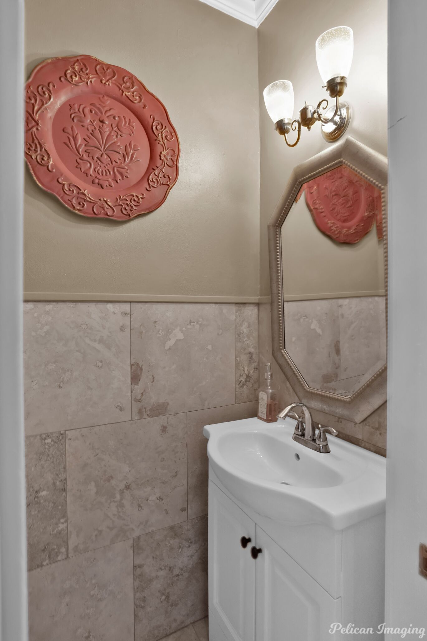 A bathroom with beige walls, a white sink, and a decorative plate on the wall.