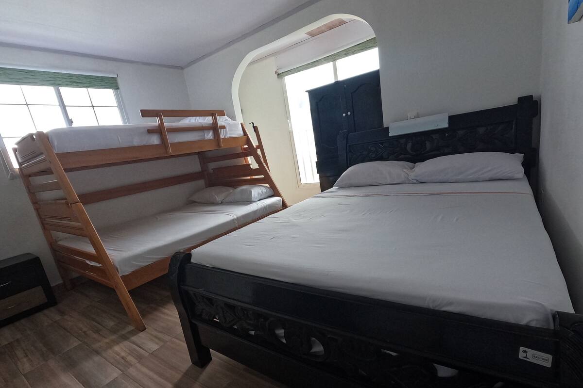 A room with a bunk bed, a single bed, a window with curtains, and a door.