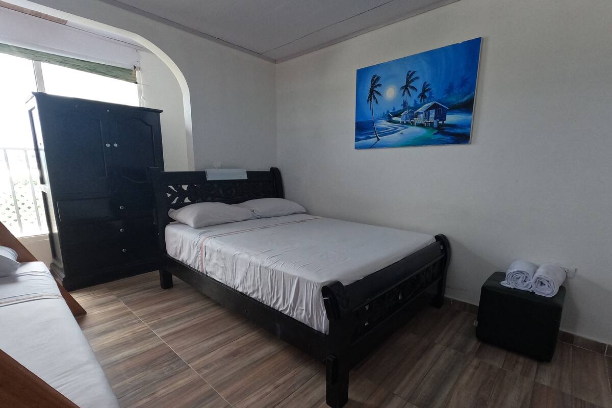 A bedroom with a bed, a wardrobe, a painting, and a small table with towels.