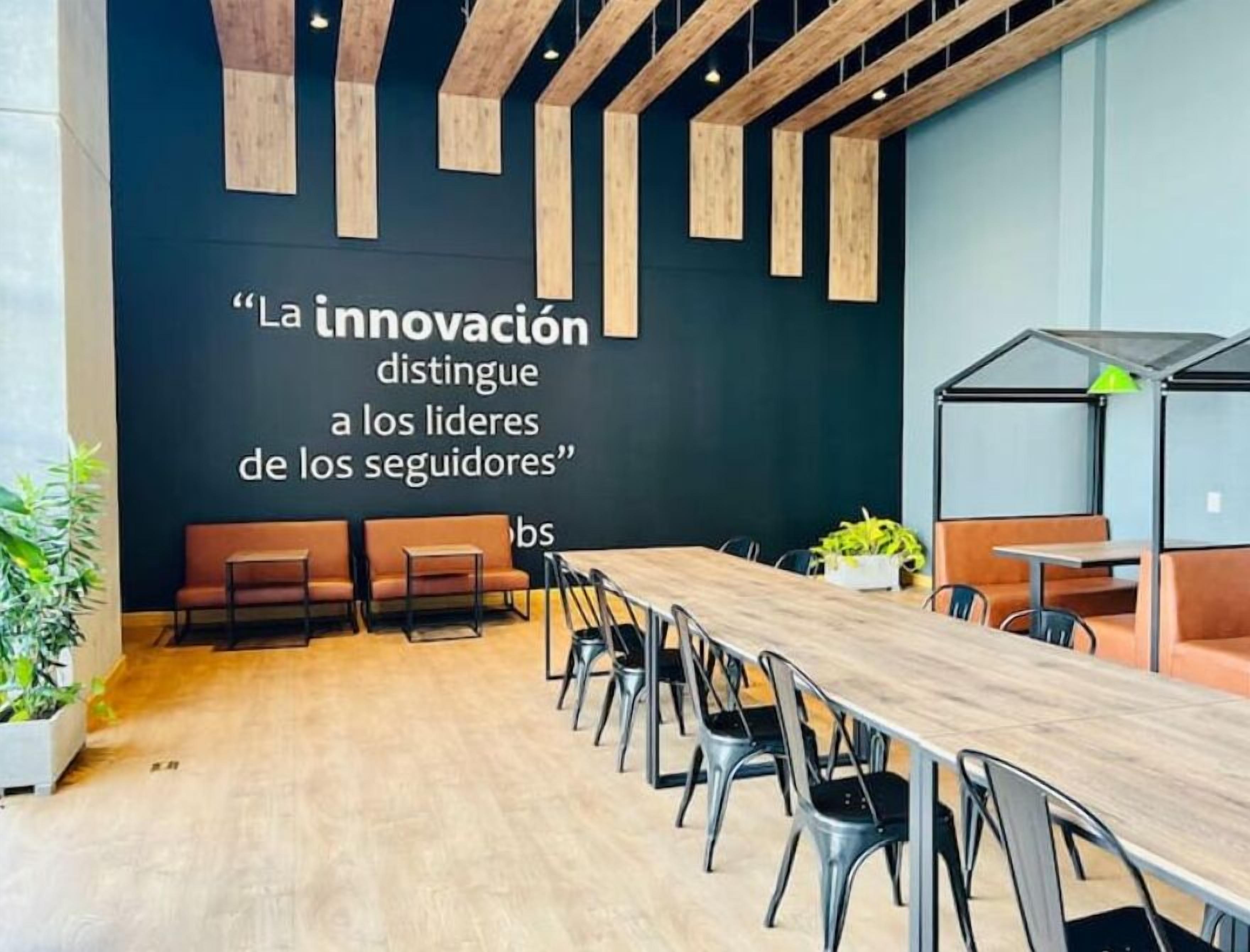 Una sala de conferencias moderna con una larga mesa y sillas, una pared oscura con una cita motivacional y vigas de madera en el techo.