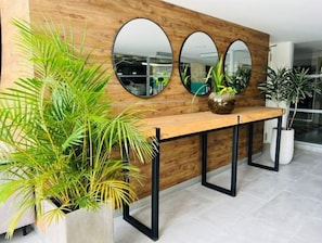 Een receptiezone met een houten wand, drie ronde spiegels, een houten receptiebalie en potplanten.
