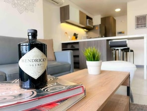 Uma garrafa de Hendrick's Gin sobre uma mesa, com uma revista, uma planta em vaso e uma cozinha moderna ao fundo.