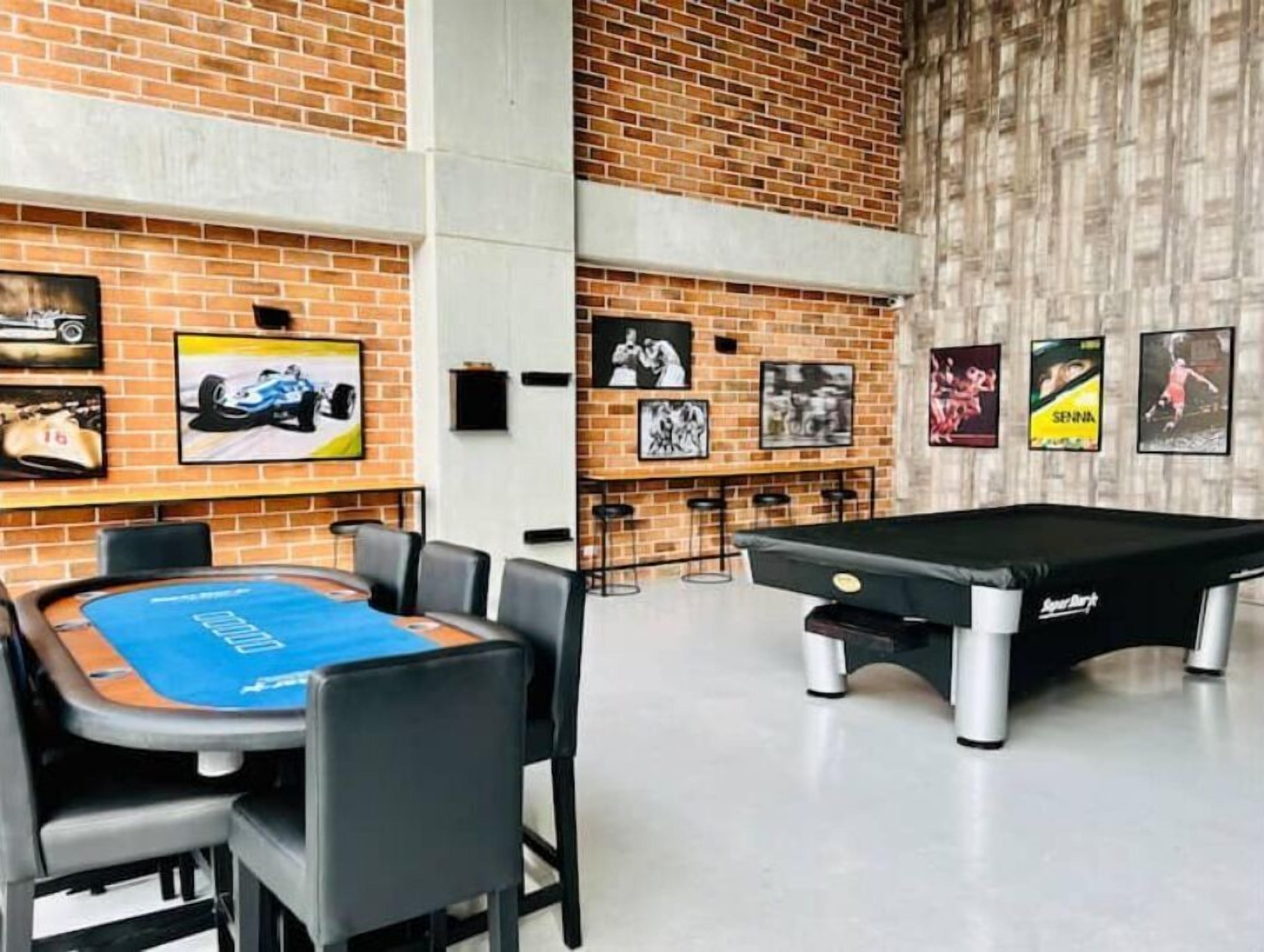 Een biljarttafel, een pooltafel en een eettafel met stoelen in een kamer met bakstenen muren en kunstwerken.