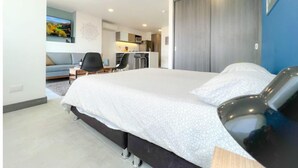 A modern hotel room with a large bed, a desk, and a kitchenette in the background. - 26th Floor A/C, Pool & Coworking (Medellín)