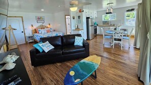 A spacious living area with a black sofa, a dining table with chairs, a kitchen in the background, and a ceiling fan. - Tree-Top Lake-Front Cottage (Madison)