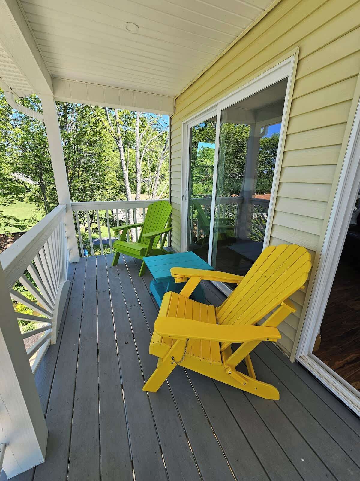 Une véranda couverte avec un plancher en bois, une balustrade blanche et une porte vitrée donnant sur une pelouse verdoyante.