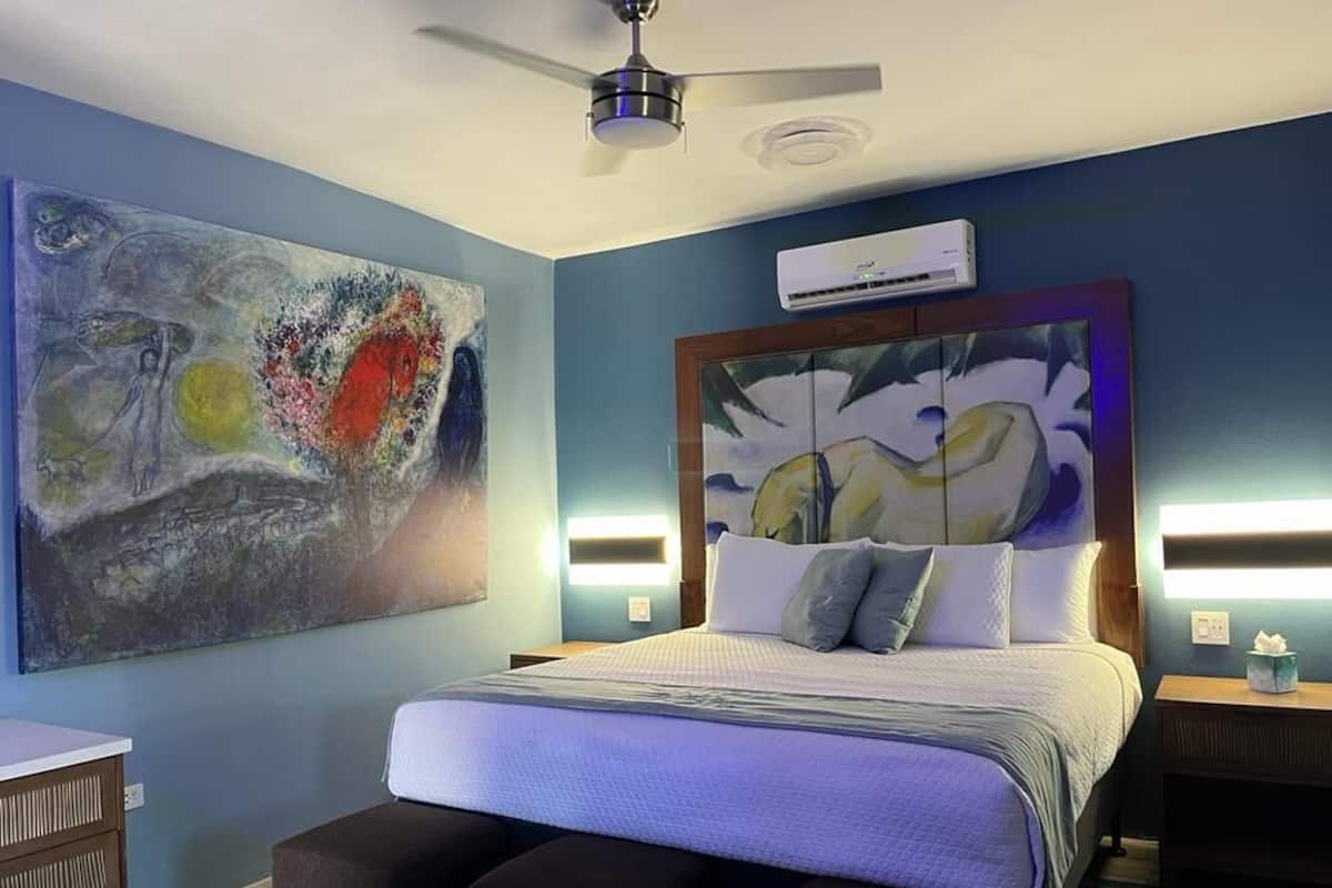 A bedroom with a bed, a ceiling fan, an air conditioning unit, and two wall-mounted lights.