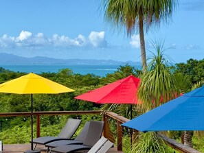 A deck with lounge chairs and colorful umbrellas overlooking a scenic view. - Old Crow Hotel and Suites (Vieques)