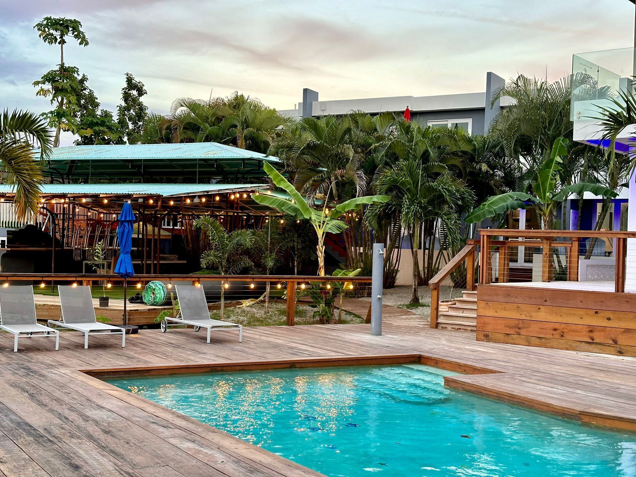 A pool area with wooden decking, lounge chairs, and a covered seating area with string lights.