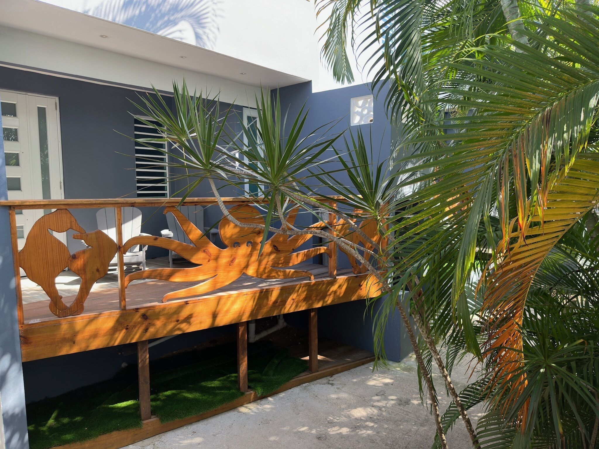 A wooden deck with a horse sculpture, surrounded by palm trees and a blue building.