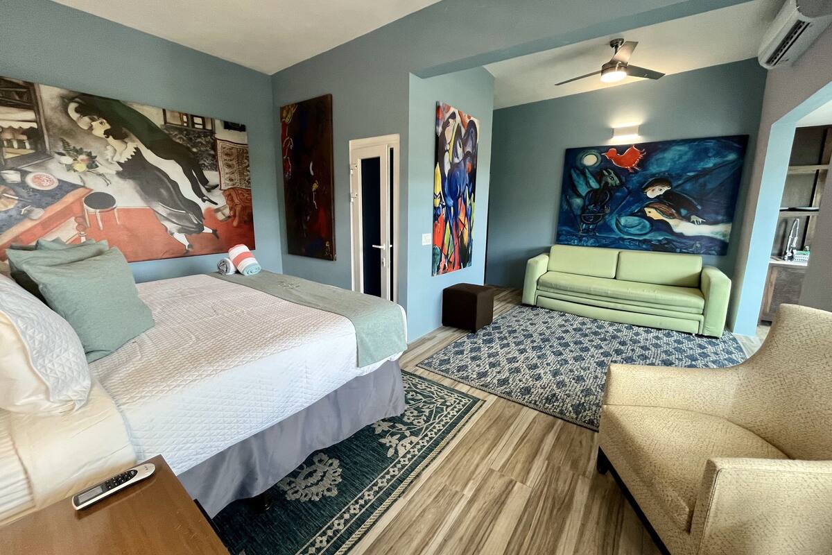 A bedroom with a bed, a green sofa, a patterned rug, and artwork on the walls.