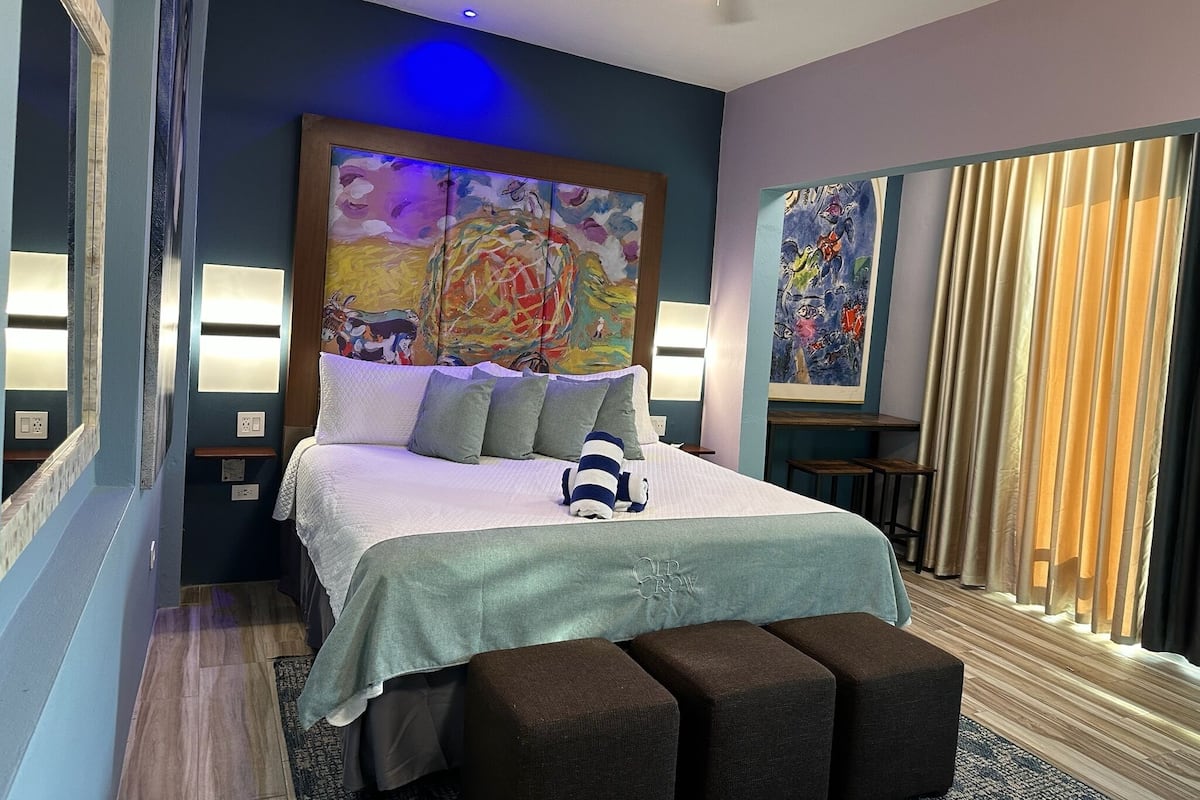 A modern hotel room with a large bed, a ceiling fan, and artwork on the walls.