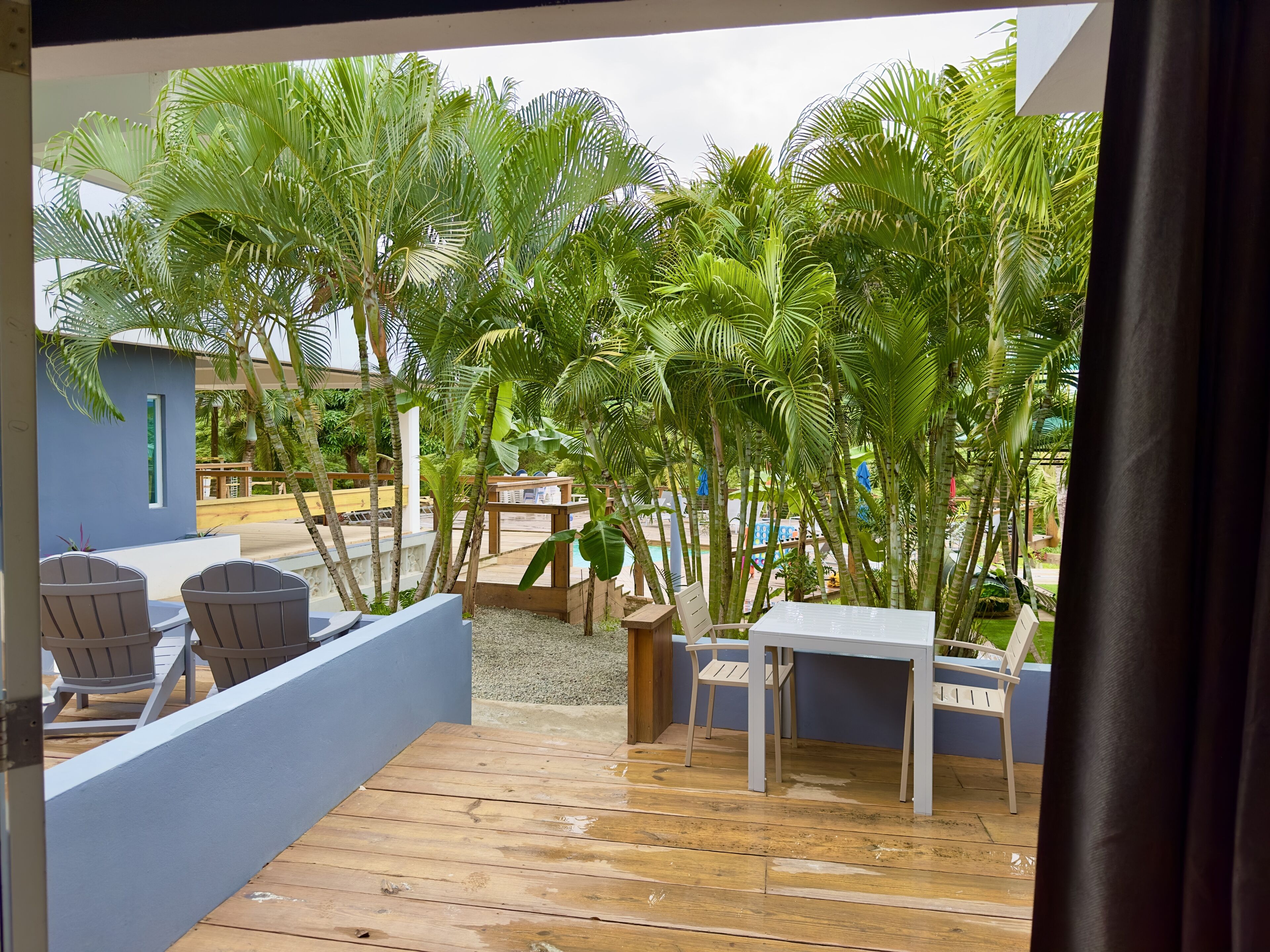 Una terraza de madera con una mesa y sillas, rodeada de exuberantes palmeras verdes.
