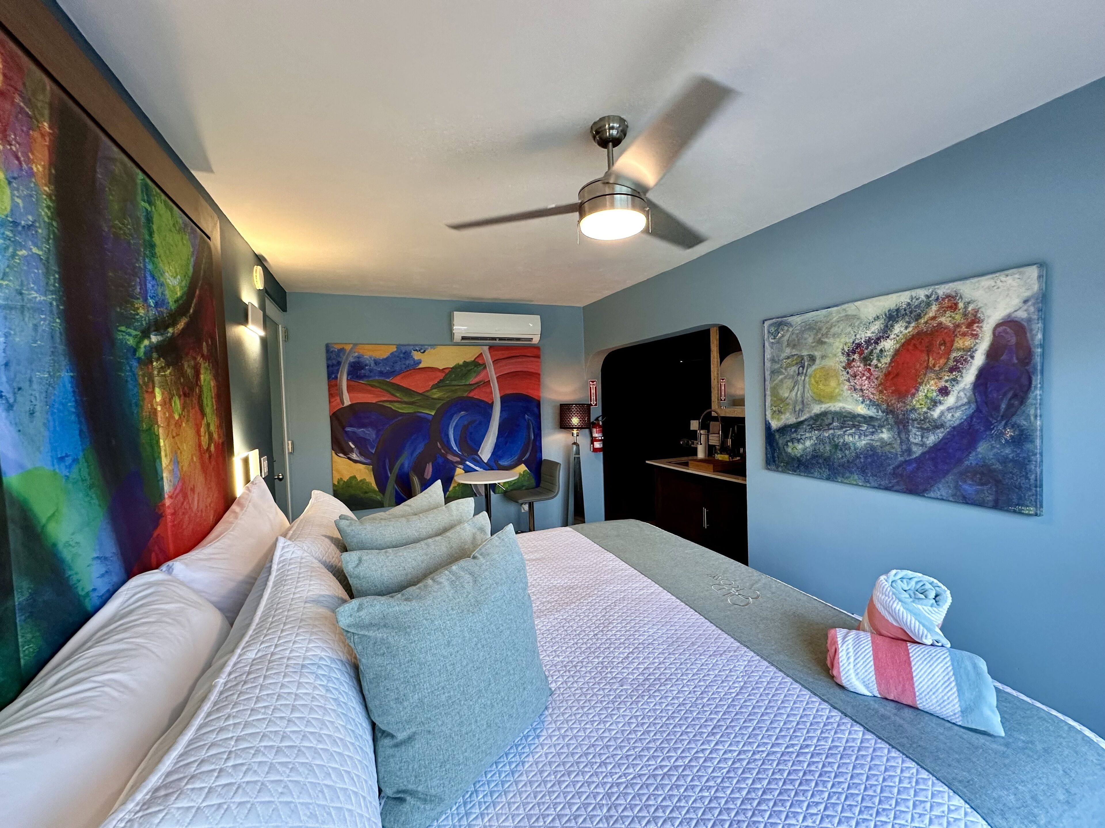 Une chambre à coucher avec un lit, des oreillers, un ventilateur de plafond et deux tableaux accrochés aux murs.