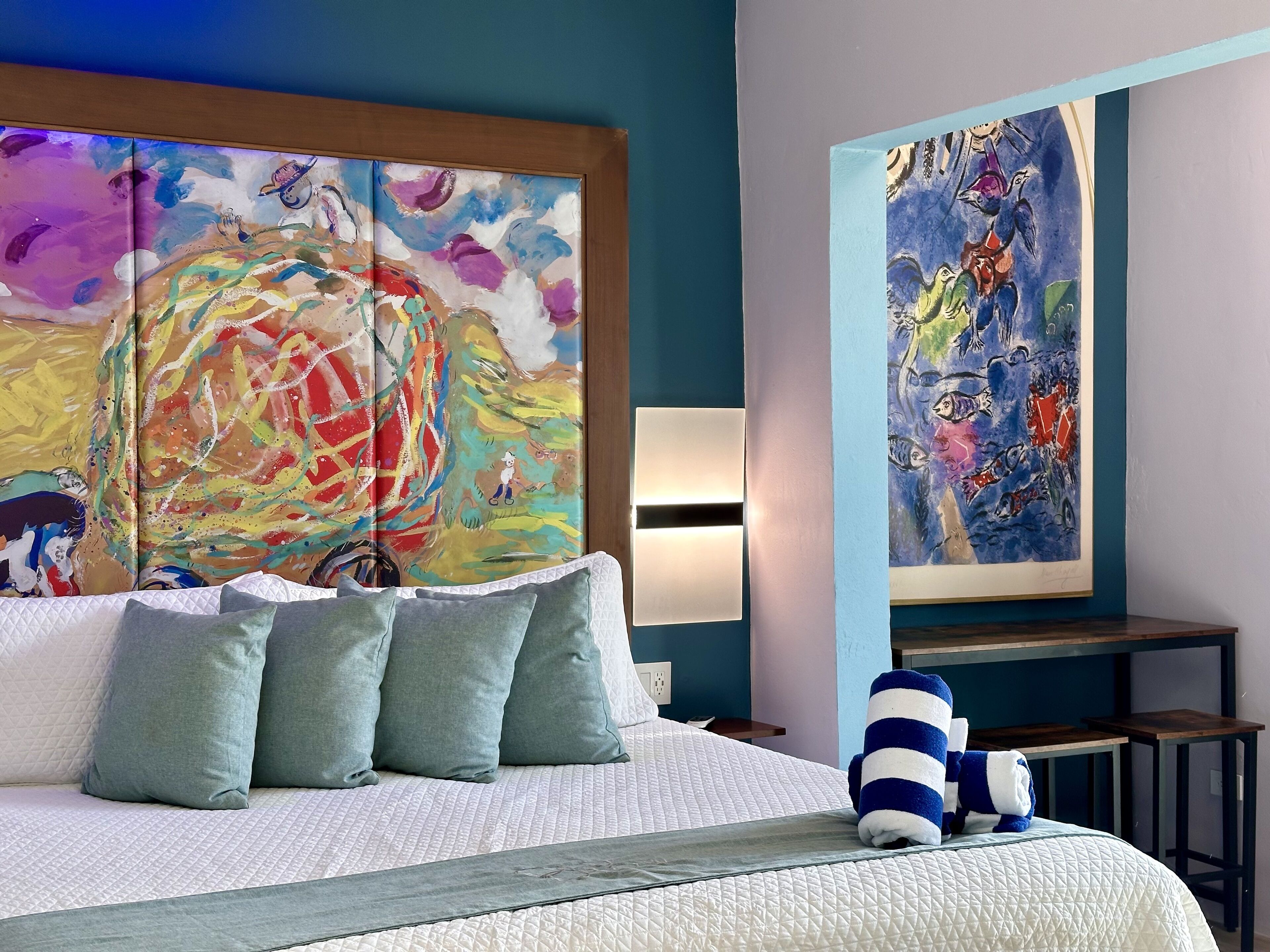A hotel room with a large bed, a painting on the wall, and a blue-striped towel on the bed.