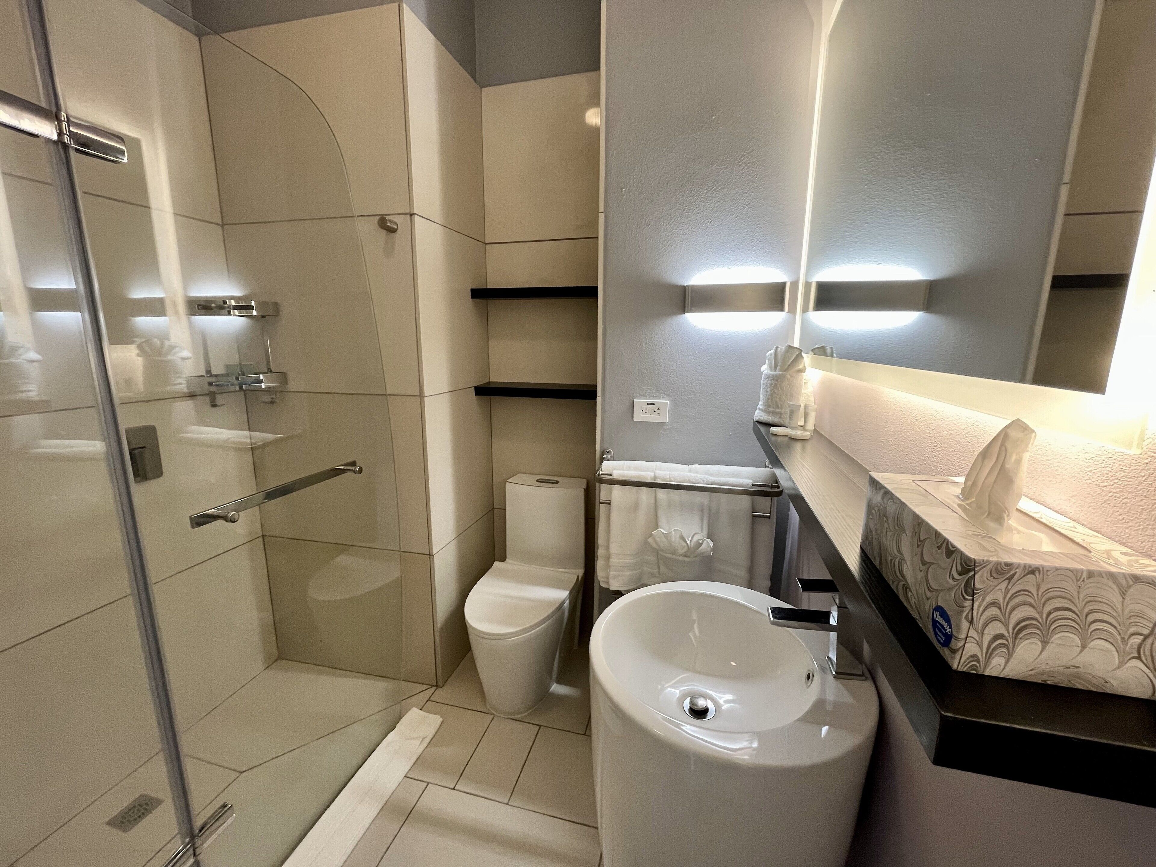 Un baño moderno con cabina de ducha de vidrio, inodoro y lavamanos con espejo.