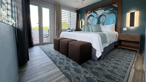 Quarto moderno com uma cama grande, ventilador de teto, quadro na parede e vista através da porta de vidro.