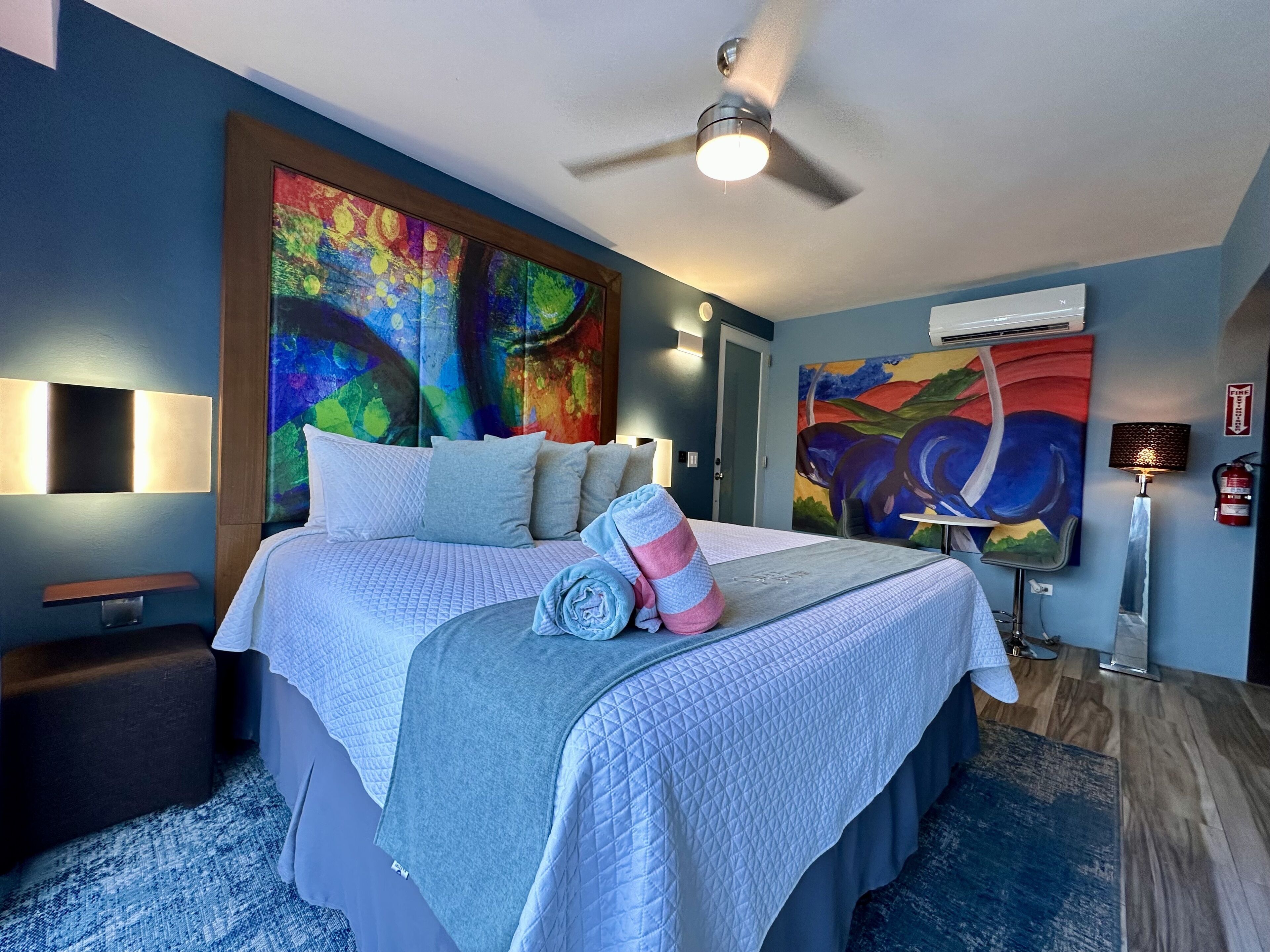 A modern bedroom with a large bed, a ceiling fan, and two abstract paintings on the walls.