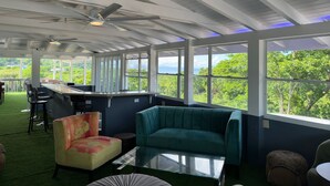 Um quarto espaçoso com teto alto, área de bar e uma grande janela com vista para vegetação exuberante.