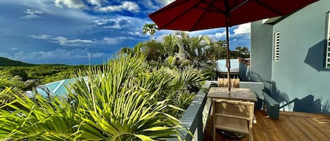 Eine Holzterrasse mit einem roten Sonnenschirm, einem Pool und üppiger Bepflanzung.