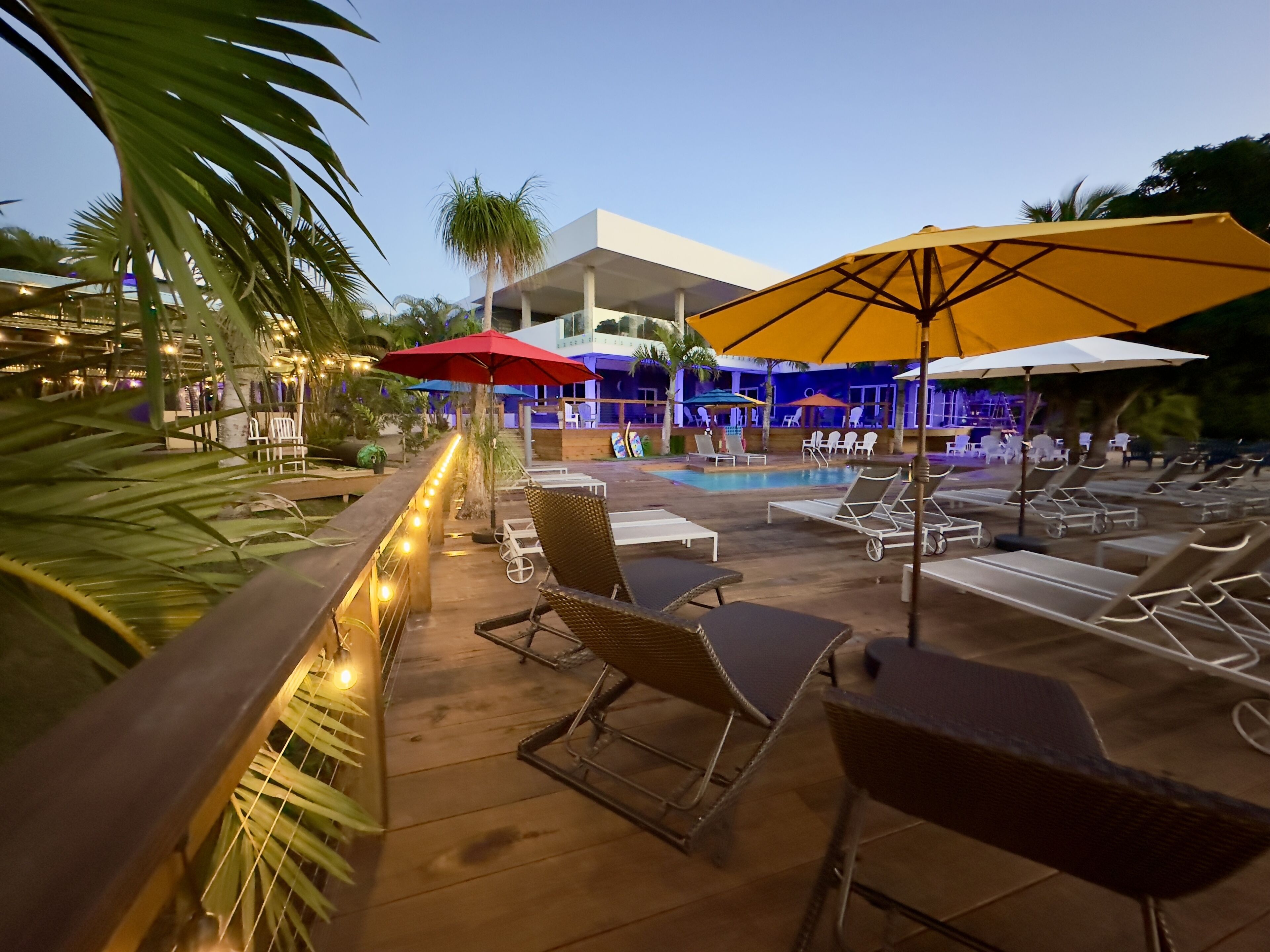 A poolside area with lounge chairs and umbrellas, a wooden deck, and string lights.
