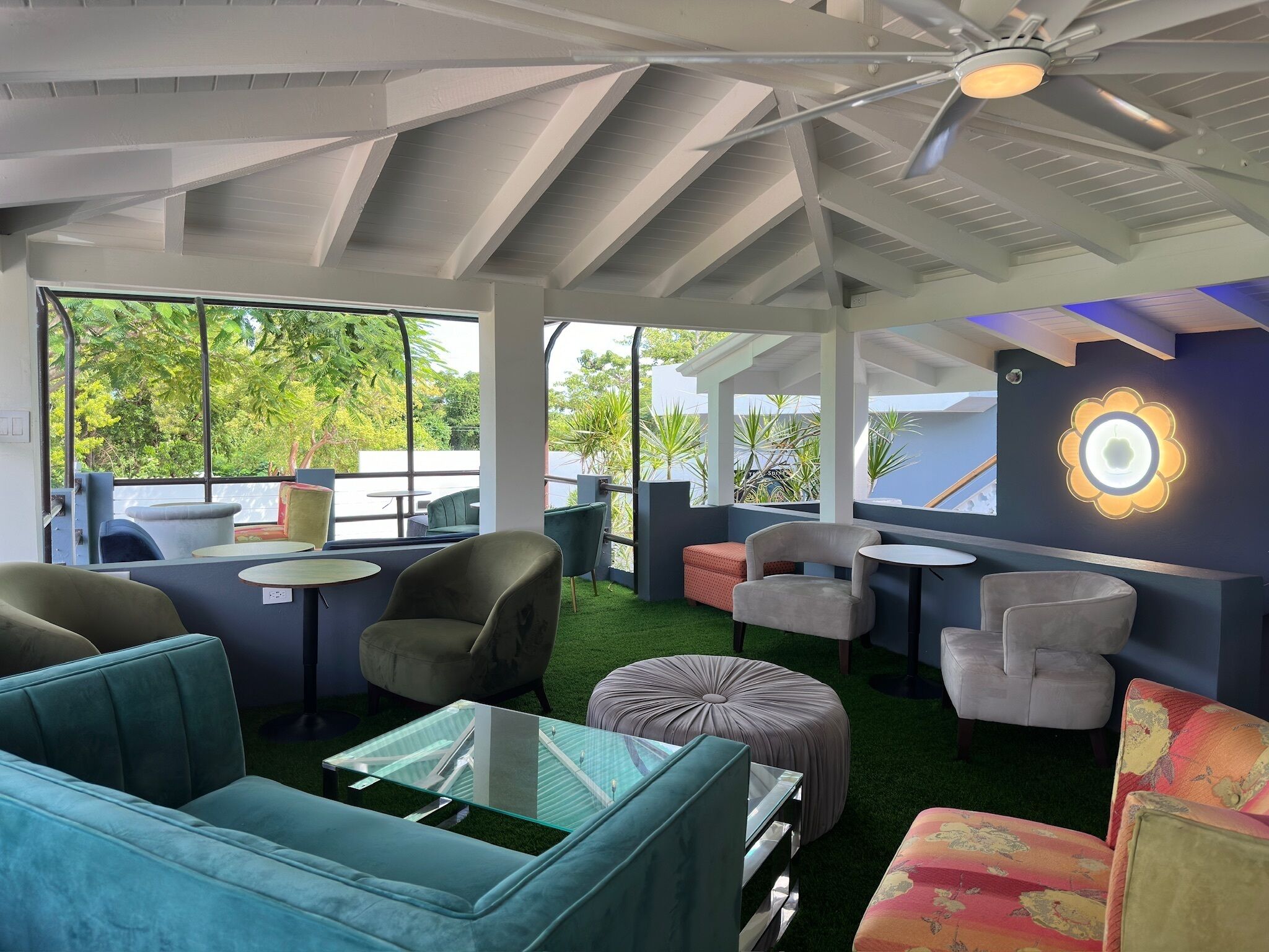 Un espace de détente moderne, doté de sièges confortables, d’un ventilateur de plafond et de grandes fenêtres offrant une vue sur la verdure.