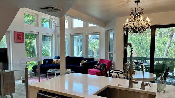 A modern kitchen with a large island, a dining area with a round table, and a living room with a dark blue sofa.