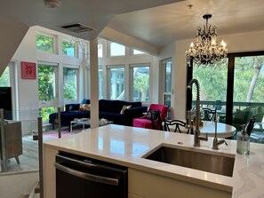 Una cocina moderna con una isla grande, un comedor con mesa redonda y una sala de estar con sofá azul oscuro.