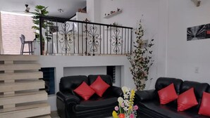 A modern living room with two black sofas, red cushions, a glass coffee table, and a staircase leading to an upper level. - Beautiful 6Bedroom 6Bath Apartment- Colombia  (Girardot)