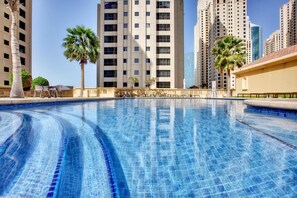 A swimming pool with clear blue water, surrounded by tall buildings and palm trees. - Spacious 1BR 5 minutes to beach (Dubai)