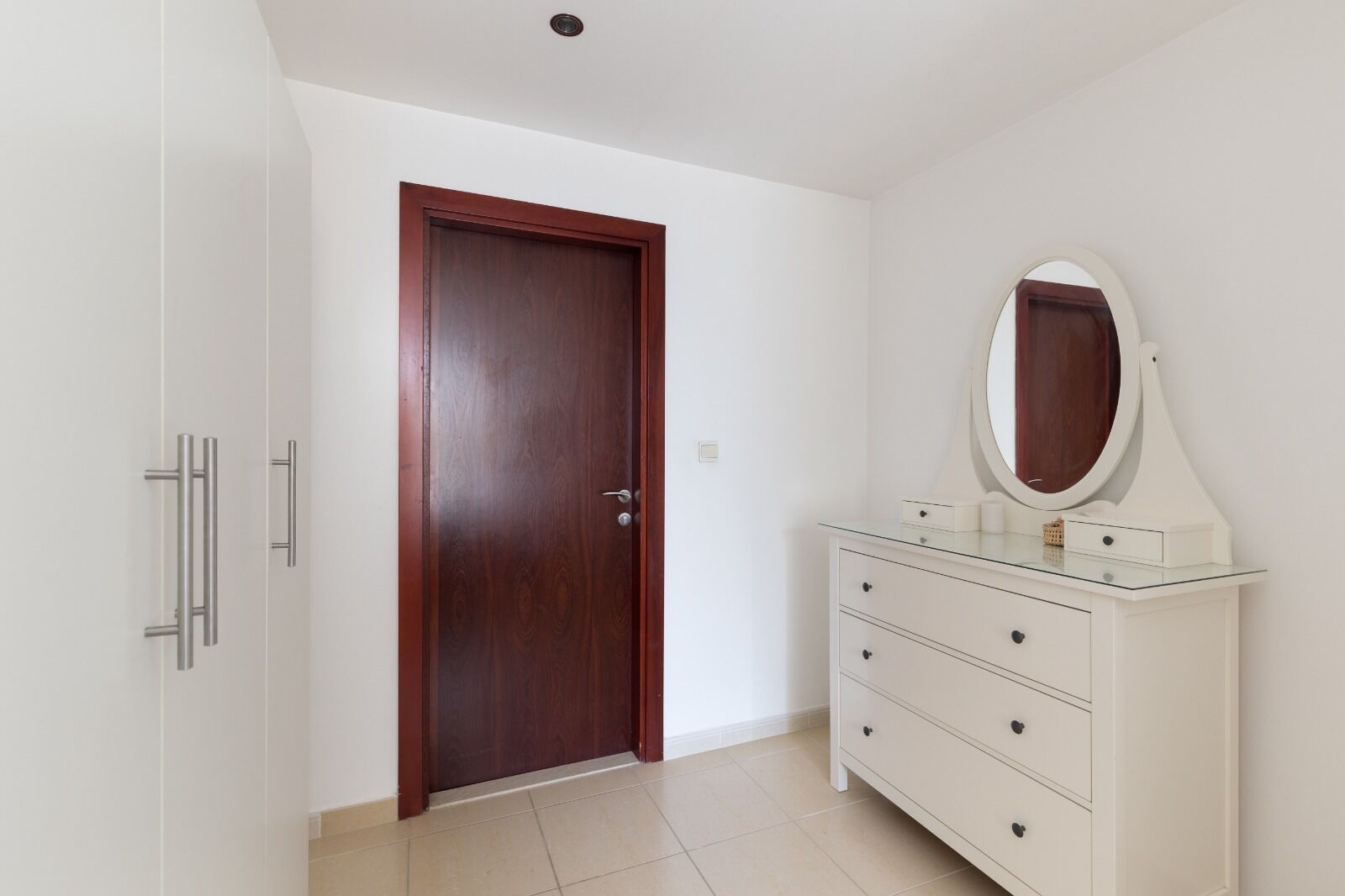 A room with a wooden door, a white dresser with drawers, and a mirror above it.