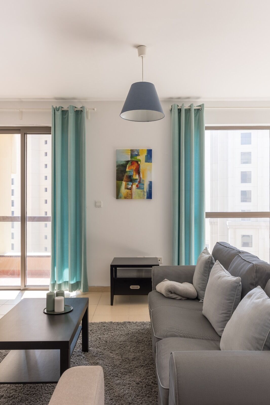 Una sala de estar moderna con un sofá gris, una mesita auxiliar negra y una lámpara colgante azul.