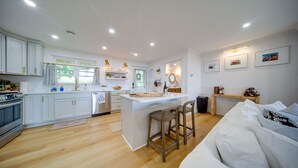Cocina moderna con armarios blancos, una isla central y un comedor con sofá y sillas.