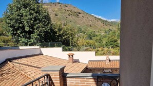 Una terraza en la azotea con una mesa y sillas, vista a una colina y un muro de ladrillo.