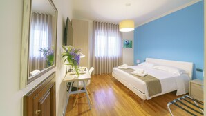 Una habitación de hotel con cama, mesita de noche, silla, escritorio y espejo.