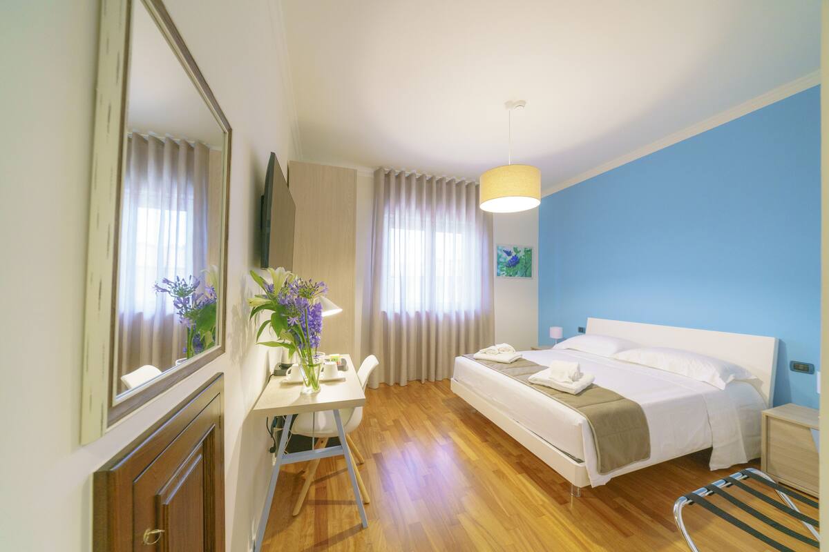 Una habitación de hotel con cama, mesita de noche, silla, escritorio y espejo.