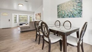 A dining area with a glass-top table, four chairs, and a modern abstract painting on the wall. - Cocohome on Water. Close to all best beaches. (Venice)