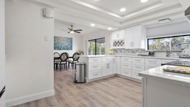 A modern kitchen with white cabinetry, a dining area with a table and chairs, and a ceiling fan. - Cocohome on Water. Close to all best beaches. (Venice)