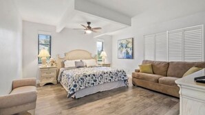 A bedroom with a bed, nightstands, a ceiling fan, a window with blinds, a couch, and a painting on the wall. - Cocohome on Water. Close to all best beaches. (Venice)