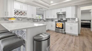 A modern kitchen with white cabinets, a central island, a stainless steel oven, and a tiled backsplash. - Cocohome on Water. Close to all best beaches. (Venice)