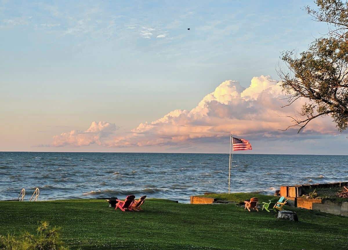 A grassy area with a flagpole and an American flag, overlooking a body of water.