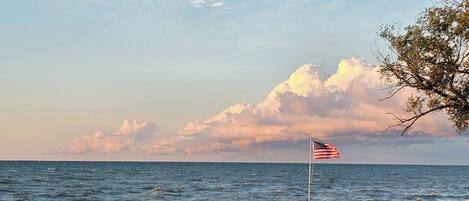 A grassy area with a flagpole and an American flag, overlooking a body of water.