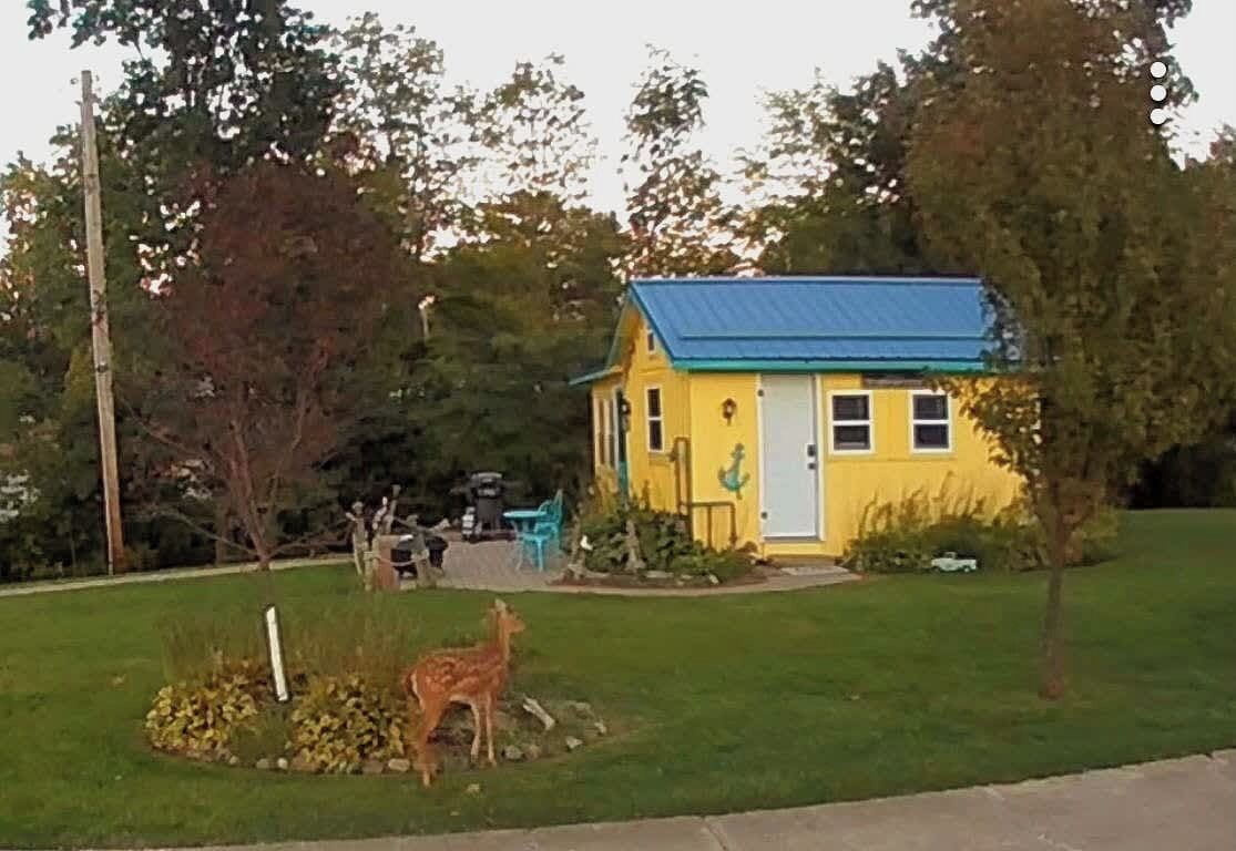Een geel huis met een blauw dak, omringd door een gazon en bomen.
