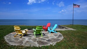 A stone patio with four Adirondack chairs in yellow, green, red, and blue, overlooking a body of water with an American flag on a flagpole.