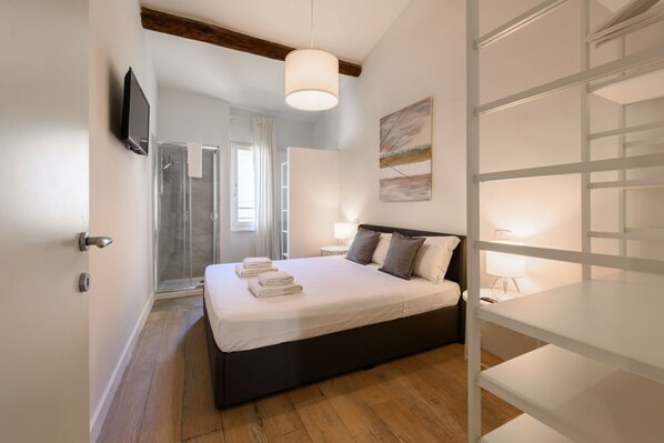 A bedroom with a bed, bedside lamps, a TV, and a shower area.