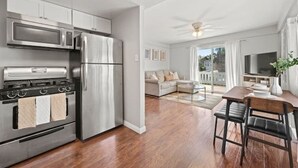 Una cocina moderna con electrodomésticos de acero inoxidable, un comedor con mesa y sillas de madera, y una sala de estar con sofá y televisor.